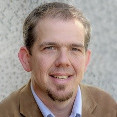 Man with a beard wearing a brown jacket and light shirt