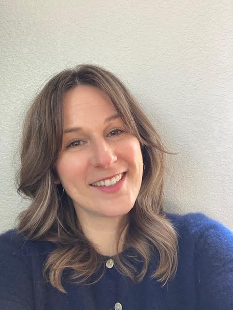 Woman with shoulder-length brown hair wearing a blue sweater against a light background